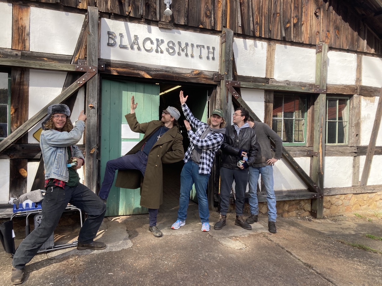 Group of 5 young individuals pointing in unison to a blacksmith sign.
