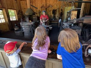 Children look on as ABANA member, Chelsea Brimer, works at the anvil.