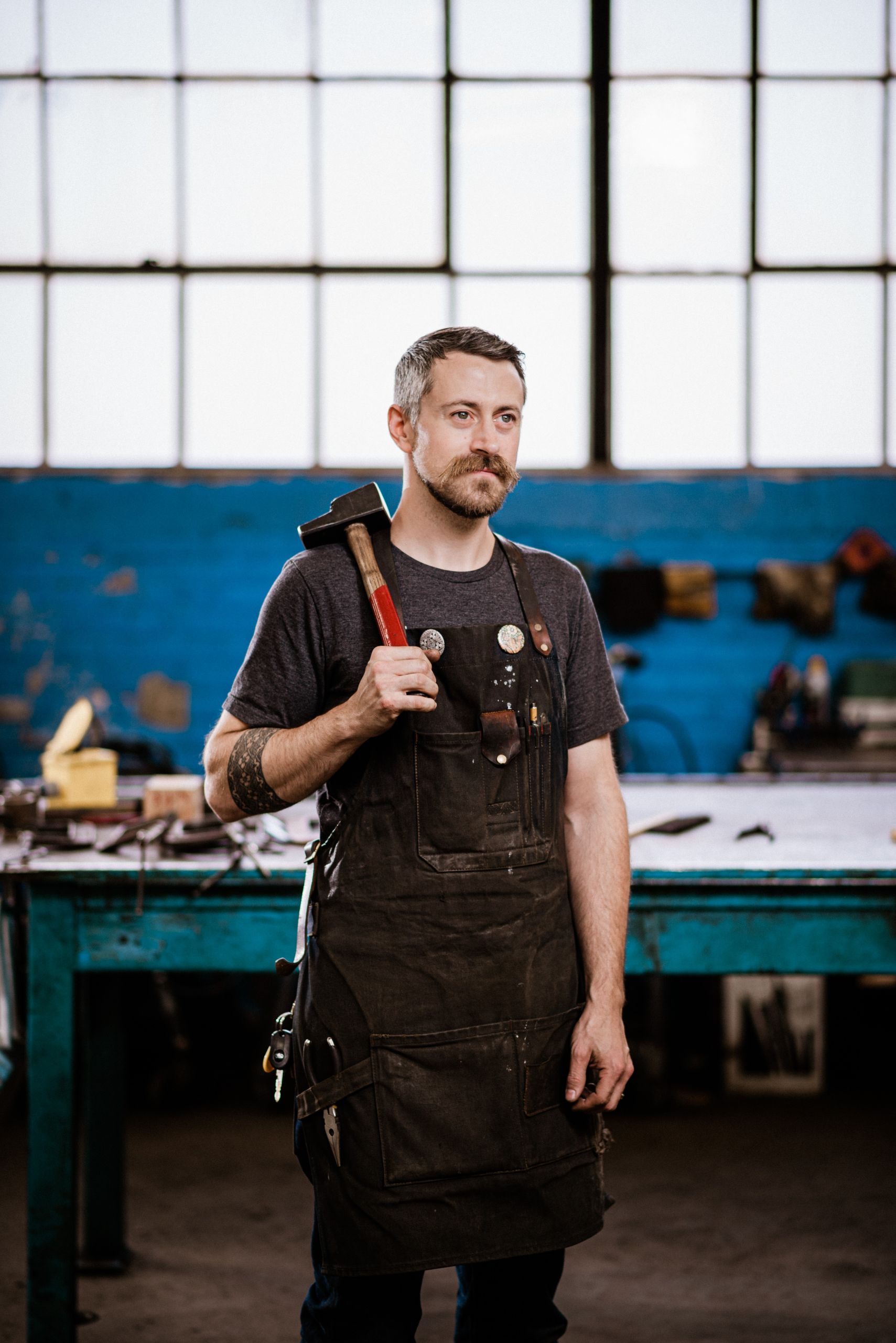 Image of blacksmith and historian, Gabriel Craig, standing in a workshop with a forging hammer in hand resting on his shoulder.